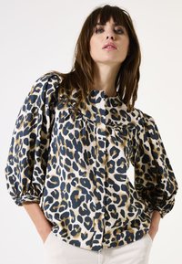 Leopardenmuster-Bluse mit einem cremefarbenen Hintergrund, Puffärmeln, durchgehender Knopfleiste und weichem Stoff. Die Details umfassen schwarze und braune Flecken.