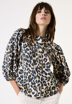 Blouse met luipaardprint op een crèmekleurige achtergrond, met pofmouwen, knoopsluiting aan de voorkant en een zachte stofstructuur. Kenmerken zijn zwarte en bruine vlekken.
