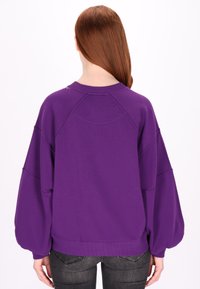 Lilla sweatshirt med overdimensionerede ærmer, ribbede manchetter og en rund halsudskæring, der fremviser en glat tekstur og sømdetaljer bagpå.