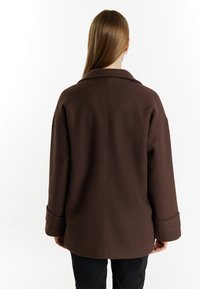 Bruine wolmix jas met een grote kraag, verlaagde schouders en brede mouwen. Glad textuur, minimale details en op maat gemaakte achternaad.