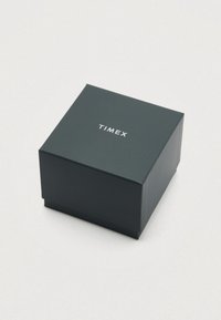 Tamsiai žalia kvadratinė dėžutė su lygia apdaila, viršuje baltais raidėmis įspaustas prekės ženklas „TIMEX“.