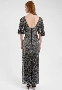 Abito da sera nero con paillettes, maniche a flutter corte, profondo scollo a V sul retro, intricate decorazioni argentate e silhouette aderente fino al pavimento.
