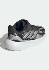 Svart och grå kamouflage sportskor med en texturerad tygövre, kardborreband och en vit gummisul med räfflade detaljer.