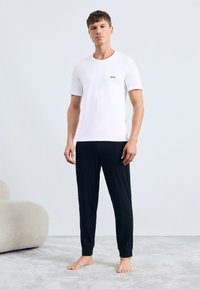 White cotton T-shirt with a black "BOSS" logo, paired with black knit joggers. The outfit is casual, featuring a relaxed fit and soft texture.