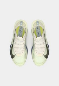 Ελαφριά αθλητικά παπούτσια σε λευκό και πράσινο, με υφή στην επάνω πλευρά, μαύρο και κίτρινο λογότυπο, κλείσιμο με κορδόνια και μπλε λεπτομέρειες.