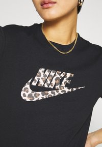 Svart bomullströja med ett leopardmönstrat Nike-logotyp i beige och brunt. Halsringningen är av typ crew, och en guldkedja är synlig.