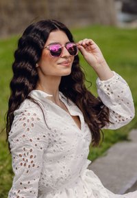 Růžové sluneční brýle s reflexními čočkami, průhlednými obroučkami a oválným tvarem, v kombinaci s bílou vyšívanou blůzou se strukturovanými výřezy.