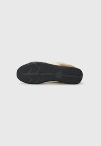 Schuhsohle mit einer strukturierten schwarzen Gummioberfläche, die ein Zickzackmuster und einen runden Akzent in der Mitte aufweist.