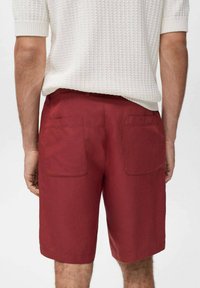 Shorts rouges en tissu résistant, dotés de deux poches arrière et d'une coupe droite. Portés avec un haut en tricot blanc texturé.