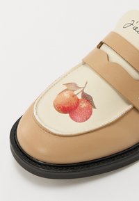 Chaussure en cuir beige avec une semelle noire, présentant un motif de cerises rouges sur un panneau crème et une sangle marron sur le dessus.