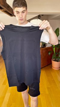 Camiseta sin mangas negra con textura suave y escote redondeado, sostenida frente a un fondo de color claro.