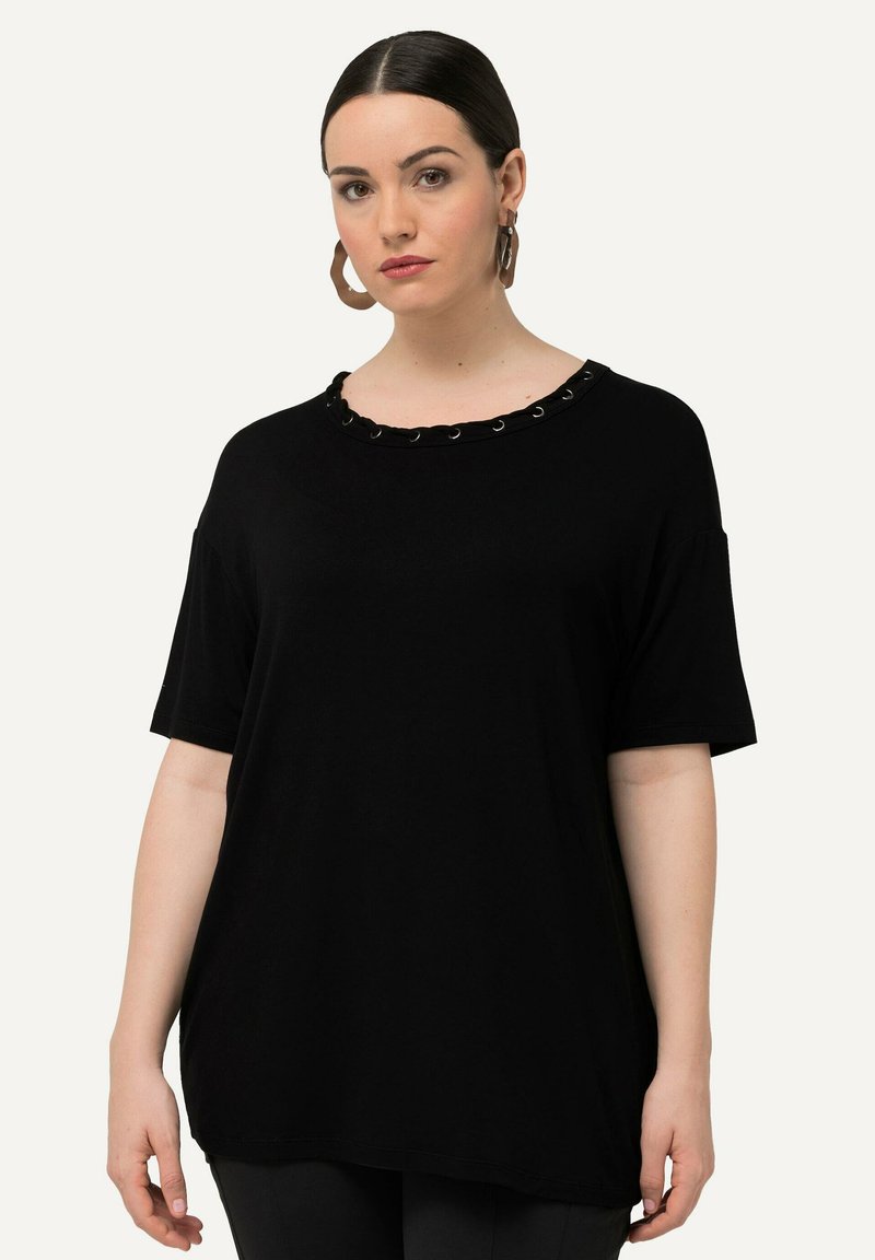 Camiseta negra de manga corta con cuello redondo, que presenta bordes con volantes y ojales decorativos de metal, confeccionada en una tela suave y lisa.