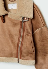 Bruine shearling jas met een beige kraag, leren accenten, ritssluiting en een zijzak. Zachte textuur met een warme uitstraling.