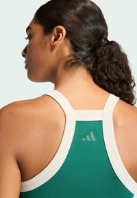 Zelený športový top s bielym lemovaním, vyrobený z textúrovanej látky a s jemným detailom loga v podobe troch pruhov na zadnej strane.