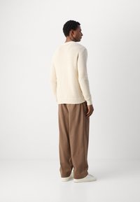Pull en crème texturé avec une coupe ample, poignets côtelés, associé à un pantalon large marron et des baskets blanches, vu de dos.