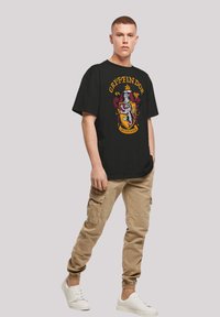 Svart bomull t-skjorte med Gryffindor våpenskjold i farger, løs passform, rund hals. Kombinert med khaki cargo-bukser og hvite sneakers.
