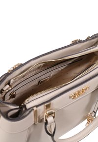 Sac à main en cuir beige avec quincaillerie dorée, comprenant deux compartiments zippés, une doublure à motifs et un design structuré.