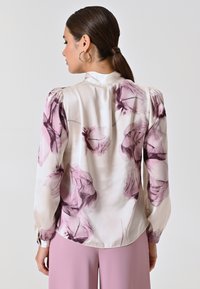 Blusa di seta con stampa floreale in tonalità di rosa e viola, con maniche a sbuffo e colletto alto. Tessuto morbido e liscio.