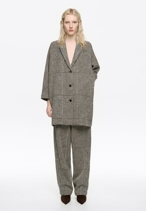 Blazer de cuadros sobredimensionado en blanco y negro, combinado con pantalones a cuadros a juego. Ambos presentan solapas grandes y botones.