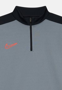 Pilkas ir juodas sportinis megztinis su ketvirčio užtrauktuku ir raudonu Nike swoosh logotipu kairėje krūtinės pusėje.
