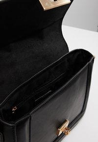 Borsa a mano in pelle nera aperta per mostrare una tasca interna con zip e chiusura a lucchetto dorato su una superficie bianca.