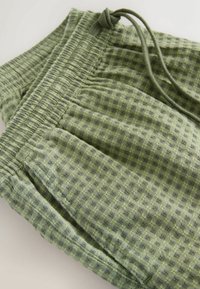 Hellgrüne Shorts aus strukturiertem Stoff mit elastischem Bund, Kordelzug und Vordertaschen, auf hellem, schlichter Hintergrund dargestellt.