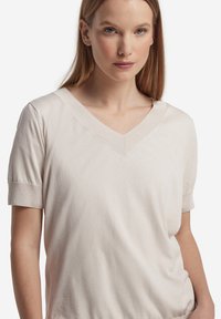 Ljusbeige kortärmad topp med V-ringning, tillverkad av mjukt tyg, med uppvikta muddar och en avslappnad passform med subtila sömmar.