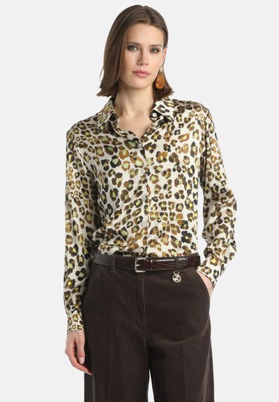 Blusa in seta con stampa leopardo, colletto classico e chiusura con bottoni; indossata con pantaloni di velluto a coste scuri e una cintura marrone texturizzata.