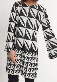 Černobílé šaty s geometrickým vzorem, kulatým výstřihem a zvonovými rukávy, vyrobené z měkké tkaniny s texturovaným povrchem.