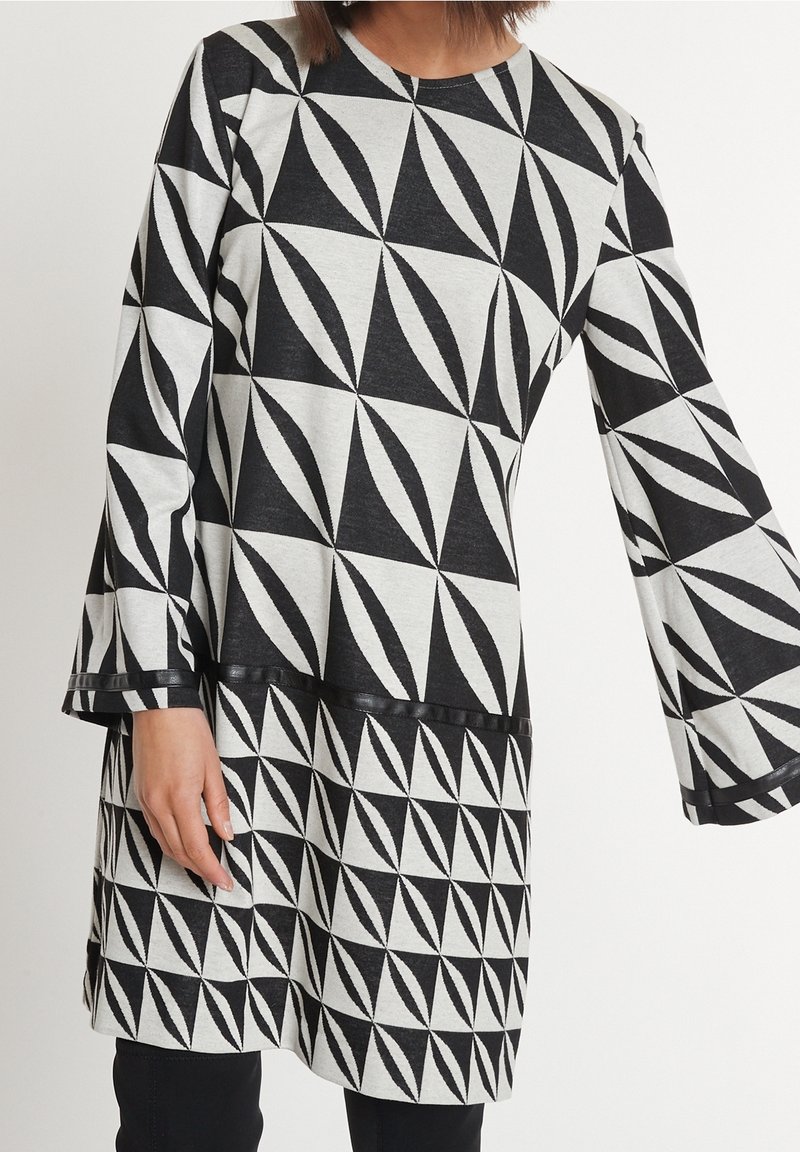 Černobílé šaty s geometrickým vzorem, kulatým výstřihem a zvonovými rukávy, vyrobené z měkké tkaniny s texturovaným povrchem.