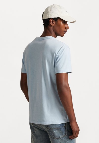 Camiseta de manga curta azul claro, feita de algodão macio, com decote redondo e um corte descontraído. Usada com calções de ganga desbotados.