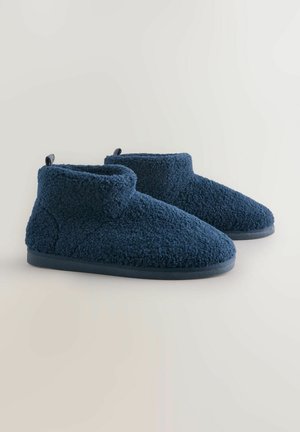 Een paar navyblauwe fleece enkelslippers met een zacht textuurweefsel en rubberen zolen op een neutrale achtergrond.