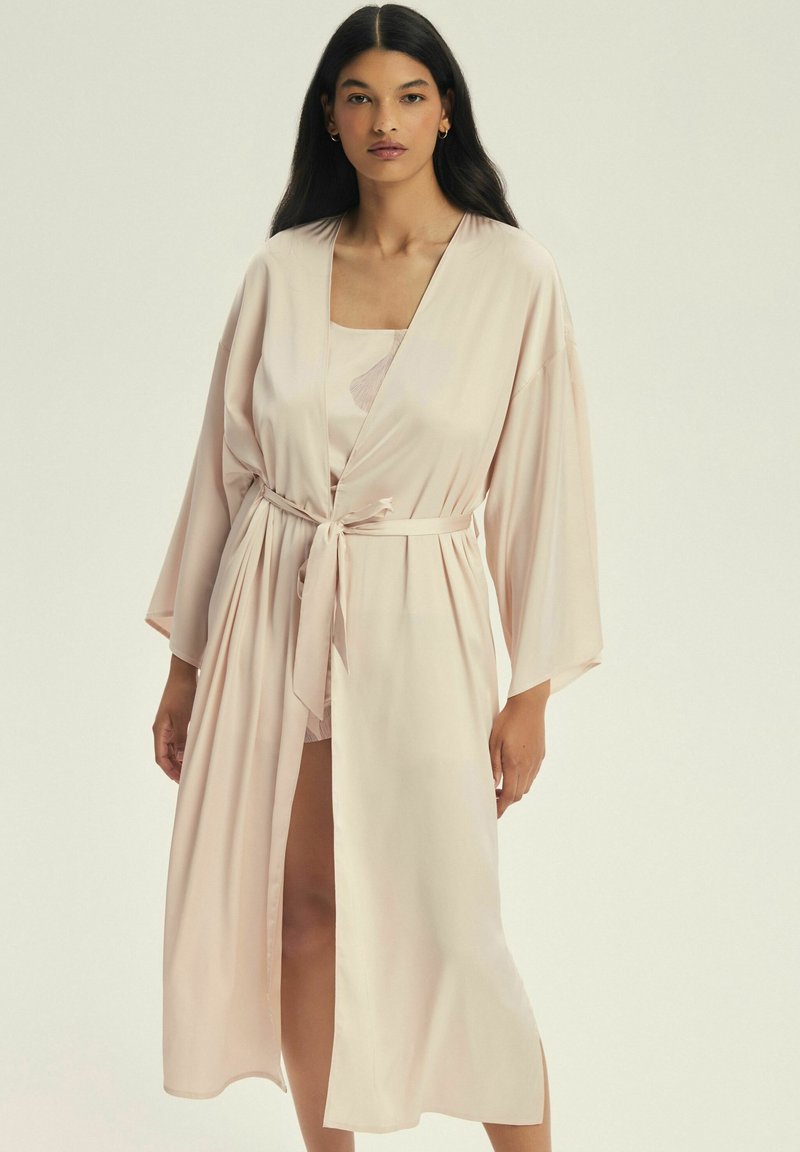 Jasnoróżowy satynowy szlafrok z szerokimi rękawami i paskiem w talii. Posiada luźny krój, sięga poniżej kolan i charakteryzuje się gładką fakturą.