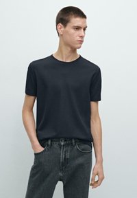T-shirt blu navy a maniche corte in cotone, con collo a rotondo. Abbinato a jeans grigi scuri, che mostrano un design minimalista.