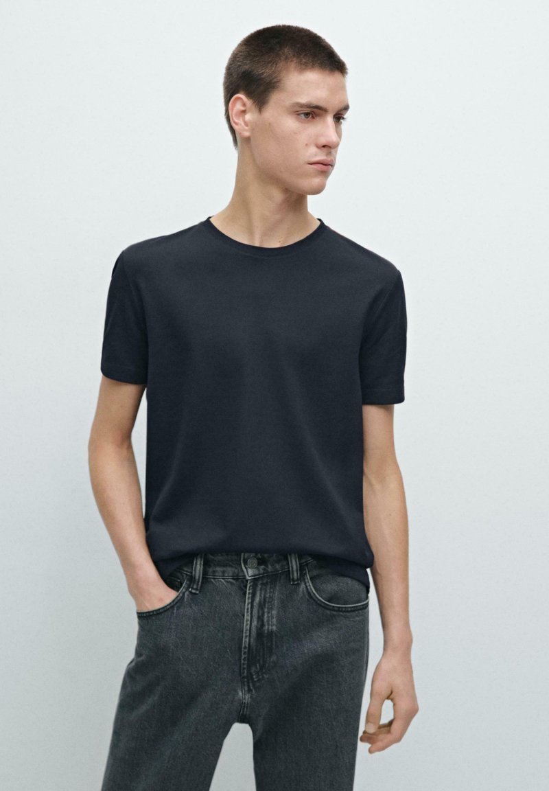T-shirt blu navy a maniche corte in cotone, con collo a rotondo. Abbinato a jeans grigi scuri, che mostrano un design minimalista.