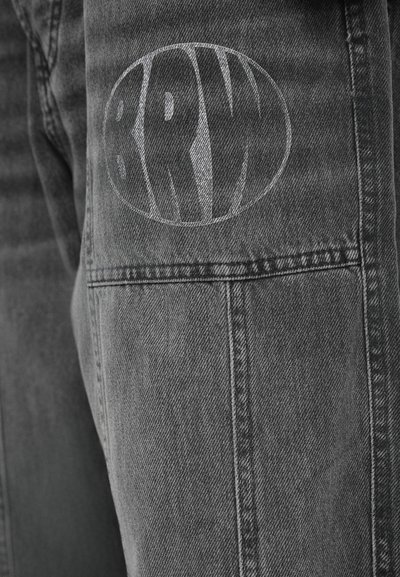Pantalons en denim gris avec une finition texturée, présentant un grand logo ovale gris clair portant l'inscription "BRW" sur le côté gauche, avec des coutures détaillées.