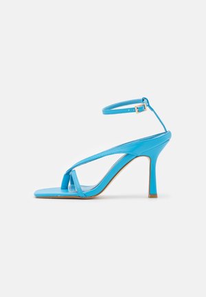 Sandale à talons hauts bleue avec fines lanières, une boucle à la cheville et un bout carré sur fond blanc.