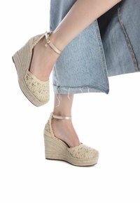 Sandalias de cuña beige con detalles de encaje, parte superior de yute trenzado, correa al tobillo y una plataforma texturizada, combinadas con culottes de mezclilla.