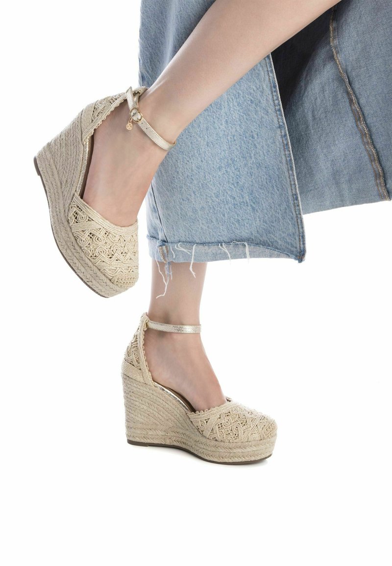 Sandalias de cuña beige con detalles de encaje, parte superior de yute trenzado, correa al tobillo y una plataforma texturizada, combinadas con culottes de mezclilla.