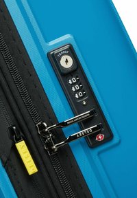 Maleta rígida azul con acabado texturizado, cremallera negra, cerradura TSA y etiqueta amarilla con el logo de Delsey. Los tiradores de la cremallera son metálicos, lo que añade contraste.
