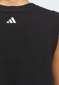 Czarny bezrękawnik z teksturowanego, siateczkowego materiału. Posiada okrągły dekolt oraz małe białe logo na plecach.