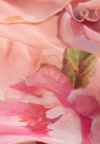 Transparentes rosa Stoff mit Blumenmuster; verfügt über eine weiche Textur und dezente Rüschen. Sichtbare Etiketten sind unter anderem "BAKER" in heller Schrift.