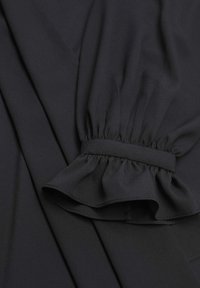 Donkere stoffen top met een gerimpelde mouw met elastische band. Zachte, gladde textuur met een consistente kleur en schone naden.