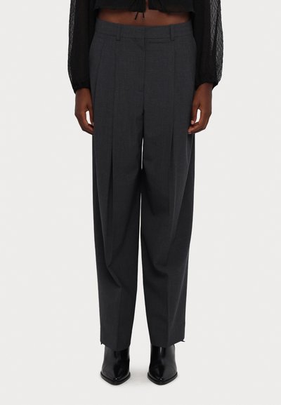 Pantalons en tissu léger de couleur grise, plissés, avec une coupe ample et un design droit, associés à des bottines noires élégantes.
