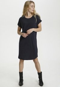 Abito blu navy a maniche corte con vestibilità rilassata, scollatura rotonda e orlo curvo. Il tessuto è liscio, abbinato a stivaletti neri alla caviglia.