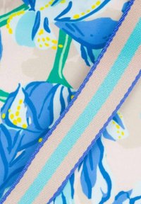Blumenstoff mit blauen und grünen Blumen sowie gelben Akzenten, übereinander geschichtet mit einem beigen und gestreiften blauen Band. Glatte Textur.