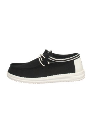 Scarpe slip-on nere in tela con suola bianca, pannello posteriore bianco a contrasto e strisce decorative. Fissate con un sistema di lacci strutturato.