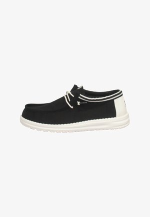 Scarpe slip-on nere in tela con suola bianca, pannello posteriore bianco a contrasto e strisce decorative. Fissate con un sistema di lacci strutturato.