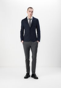 Navy blazer with two buttons, gray dress pants, and a light shirt, paired with a gray tie and black shoes. Smooth fabric with tailored fit.