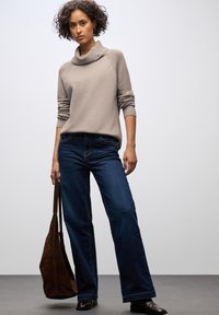 Ljust beige stickad tröja med polokrage, mörkblå raka jeans och en brun mockaväskan över axeln. Slät textur och avslappnad passform.